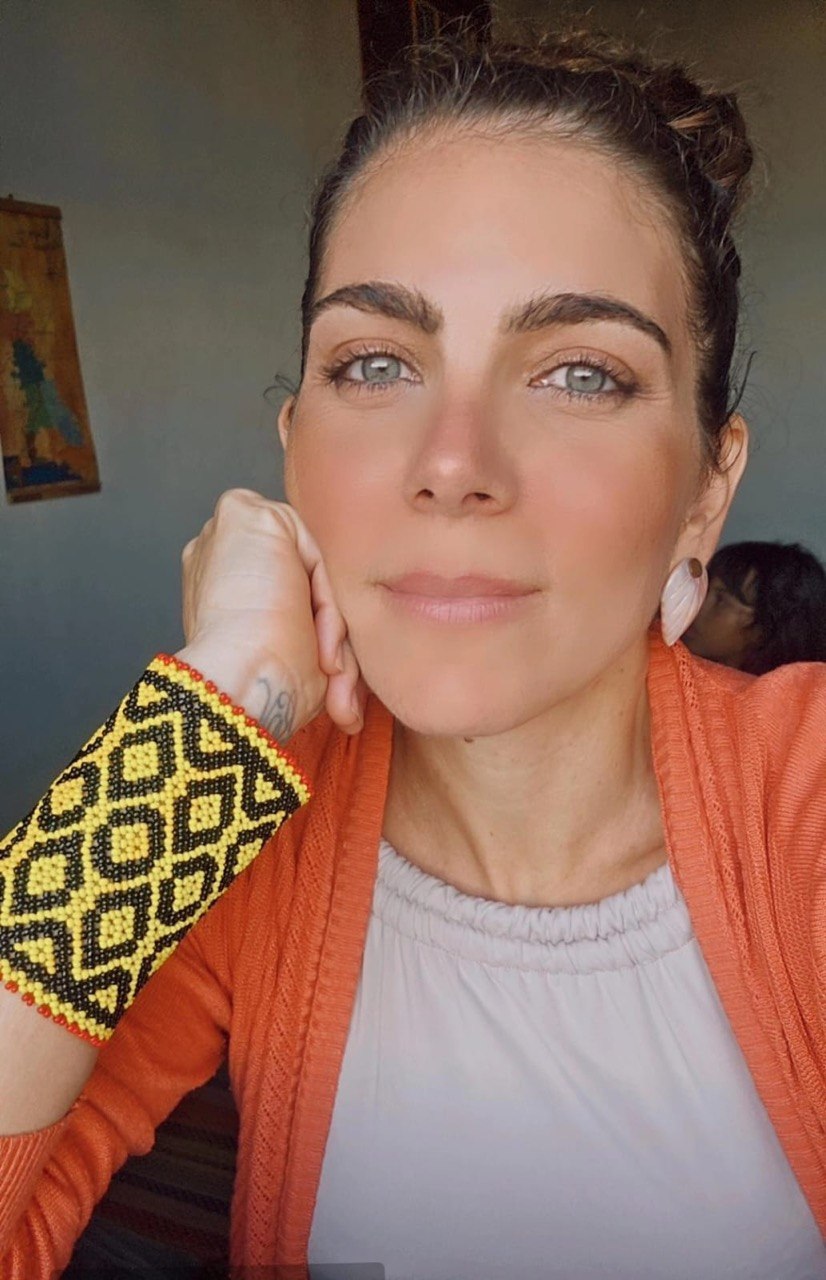 Flávia Maitri em ambiente doméstico, usando pulseira de miçanga artesanal